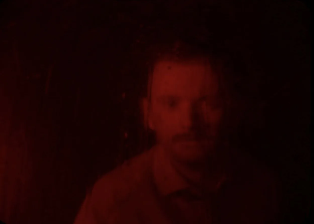 The Holy Yield — man behind rain-streaked glass in red light